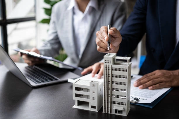 two people conversing, holding a pen, miniature building on the table -real estate developers