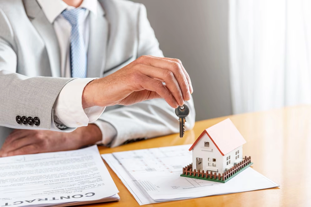 person holding key on paper and miniature house -real estate promotion