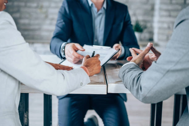 3 people conversing with paper and pen on table -real estate business