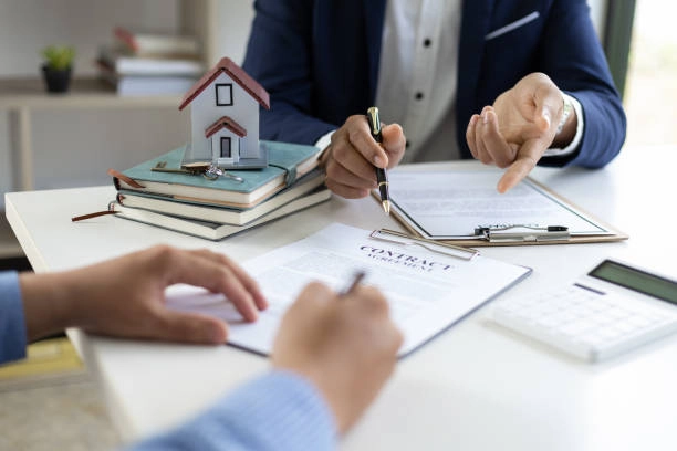 2 people conversing with contract papers, pen and miniature house -real estate definitions