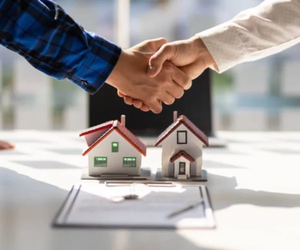 hands shaking with small house and paper on table -real estate consulting