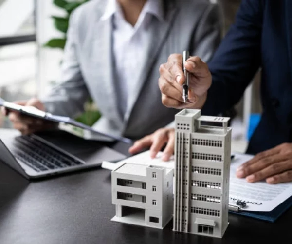 two people conversing, holding a pen, miniature building on the table -real estate developers