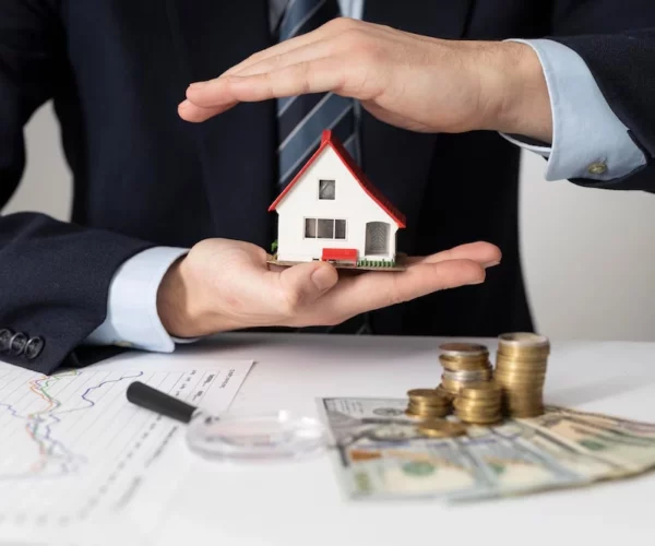 miniature house person holding with money on top of paper -real estate finance