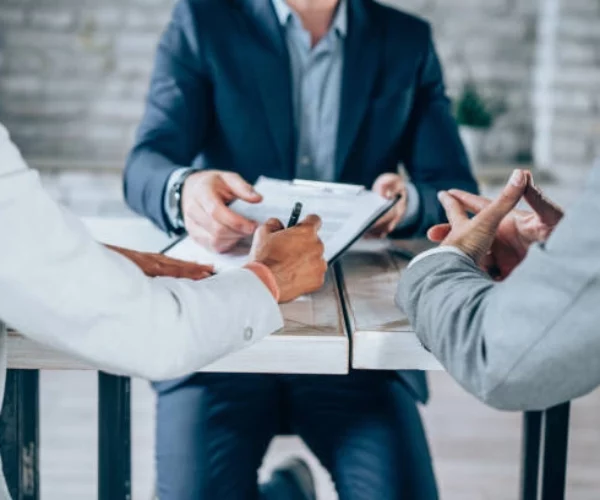 3 people conversing with paper and pen on table -real estate business