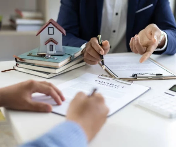 2 people conversing with contract papers, pen and miniature house -real estate definitions